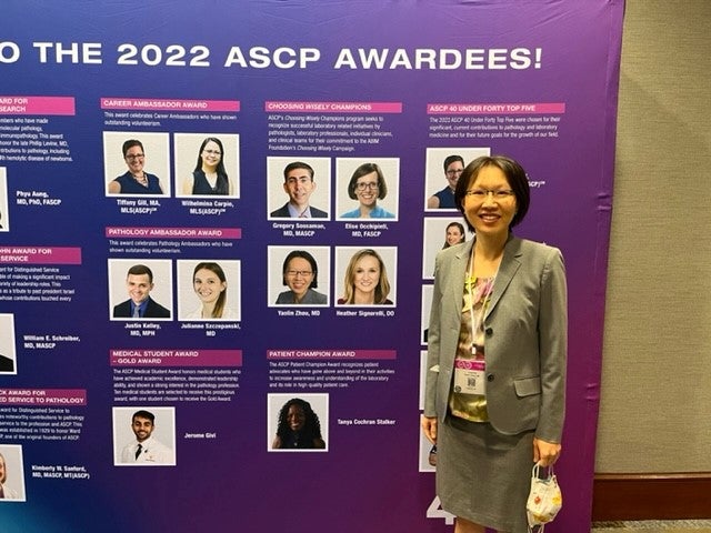 Dr. Zhou standing in front of a sign that reads "The 2022 ASCP Awardees!"