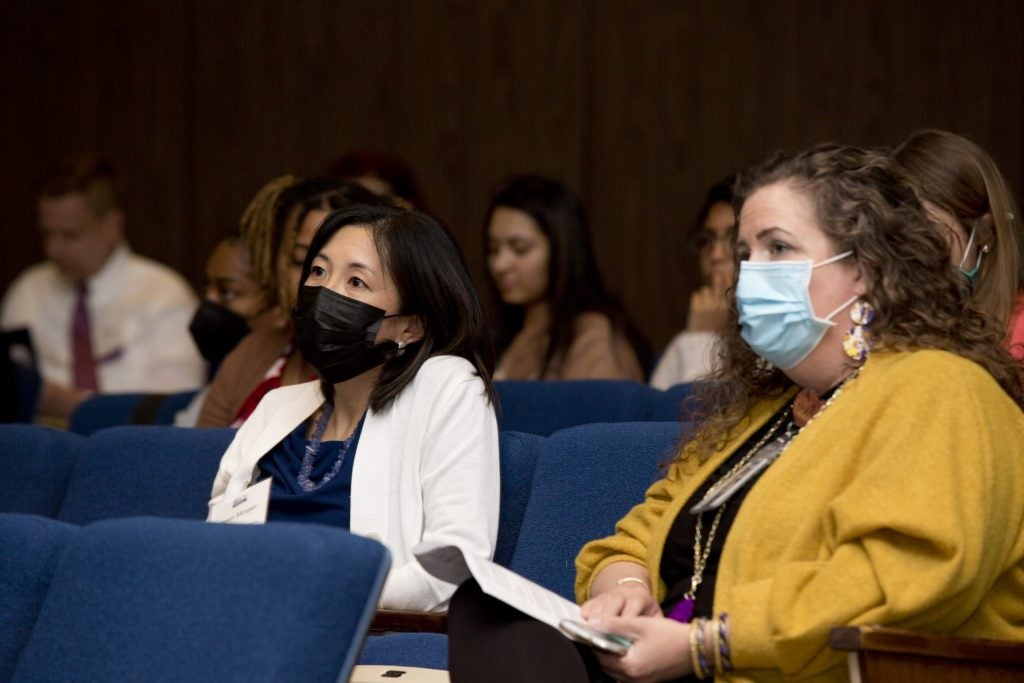 Closeup of two women wearing face masks sitting in an audience in an auditorium.