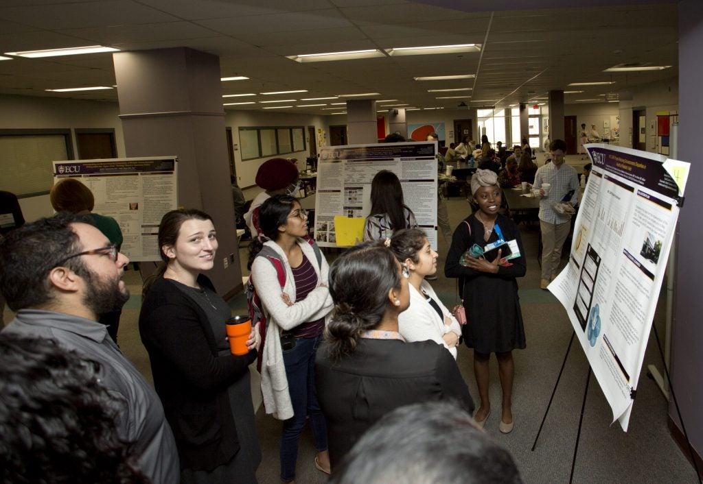 A diverse group of people looking at posters on display in a large room.