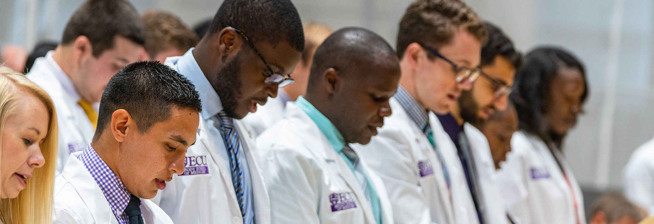 Row of Doctors looking down, reciting something.